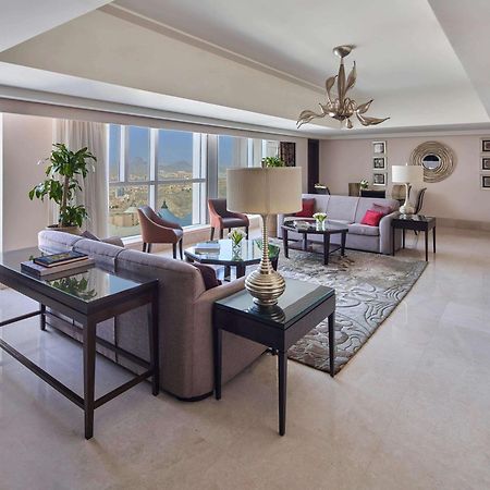 Makkah Clock Royal Tower, A Fairmont Hotel La La Mecca Esterno foto The photo shows a spacious, elegantly designed living room. It features large windows that allow natural light to flood the space and provide a view of the city. The room has a mix of comfortable seating arrangements, including a light-colored sofa s