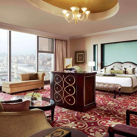 Makkah Clock Royal Tower, A Fairmont Hotel La La Mecca Esterno foto The photo shows a luxurious hotel room featuring elegant decor. The spacious room includes a large bed with plush bedding, a stylish seating area with a sofa, and a coffee table. There is a visually striking area rug on the floor, adding warmth and c