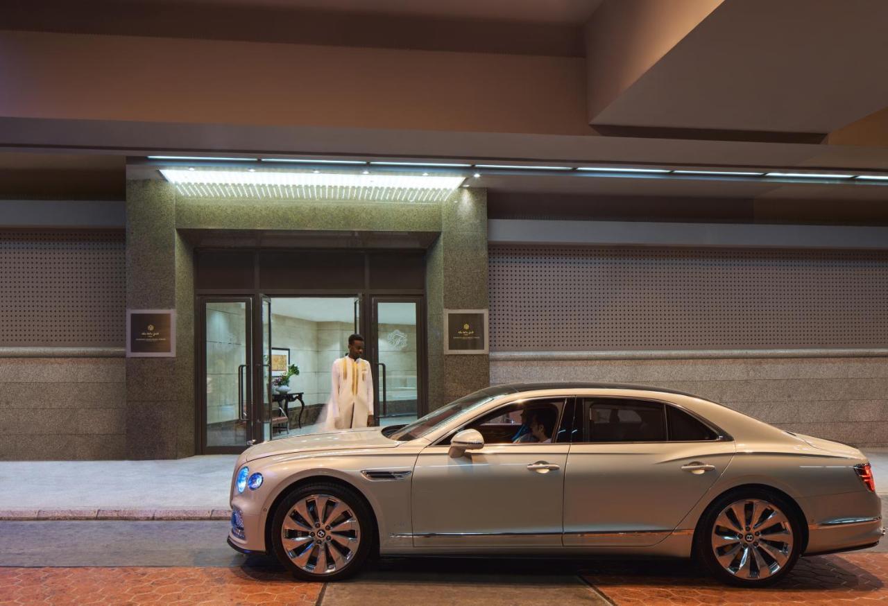 Makkah Clock Royal Tower, A Fairmont Hotel La La Mecca Esterno foto The photo shows a luxurious silver car parked outside a modern building entrance. There is a doorman in uniform standing in front of the entrance, which has a sleek, contemporary design. The setting appears upscale and elegant, suggesting a high-end 