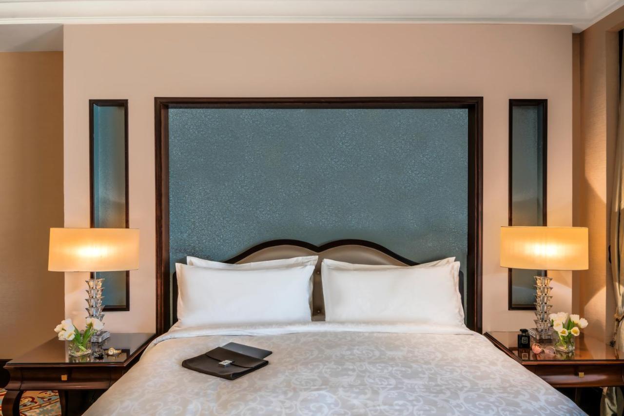 Makkah Clock Royal Tower, A Fairmont Hotel La La Mecca Esterno foto The photo displays a cozy hotel room, featuring a large bed with white bedding and two pillows arranged neatly. Behind the bed, there is a stylish headboard with a textured blue panel and dark wooden trim. On either side of the bed, there are nightst