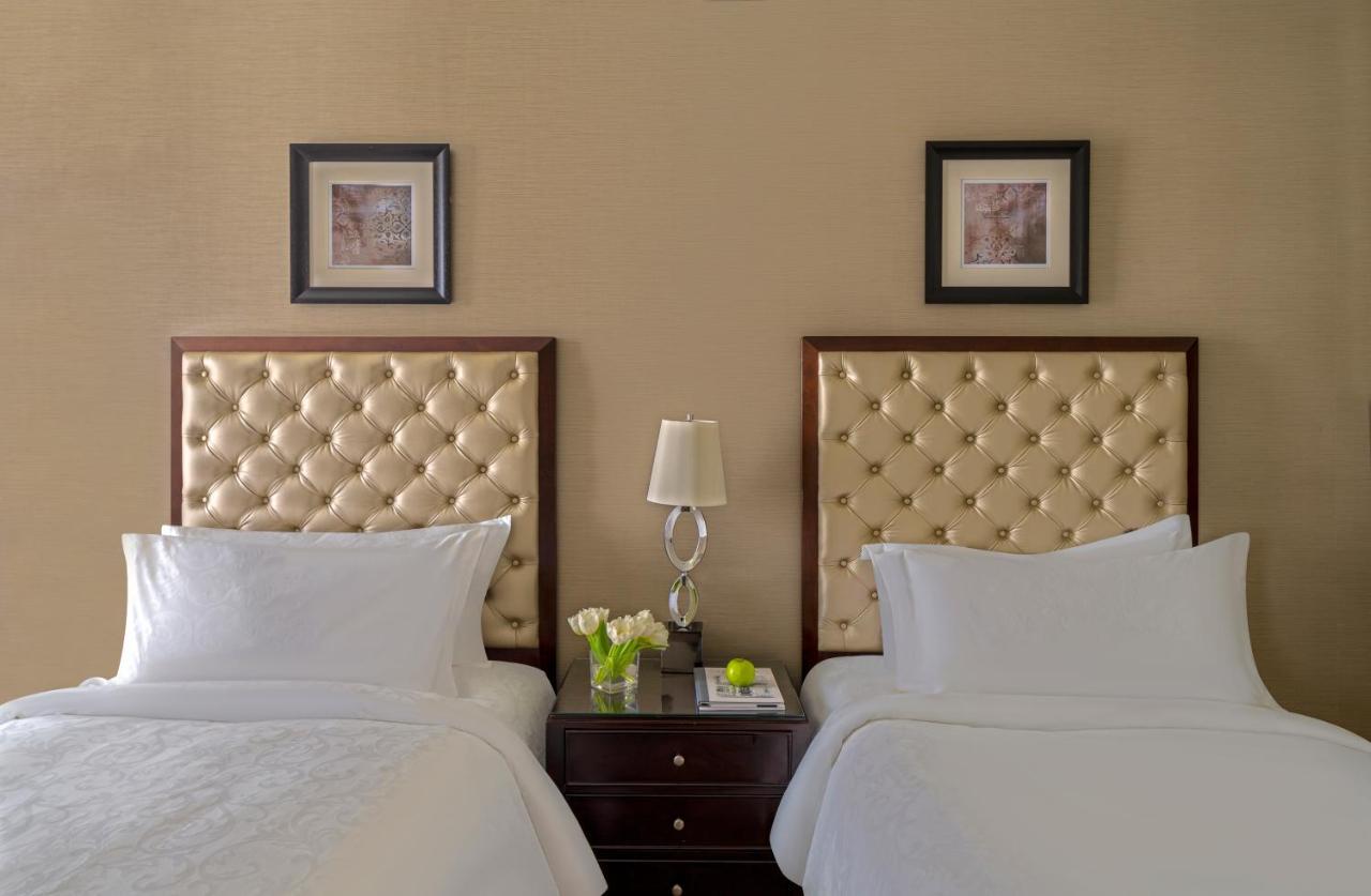 Makkah Clock Royal Tower, A Fairmont Hotel La La Mecca Esterno foto The photo shows a cozy and elegant hotel room with two twin beds. Each bed has a tufted, light-colored headboard framed in dark wood. Between the beds is a small nightstand with a decorative lamp and a small vase containing flowers. Above each bed, t