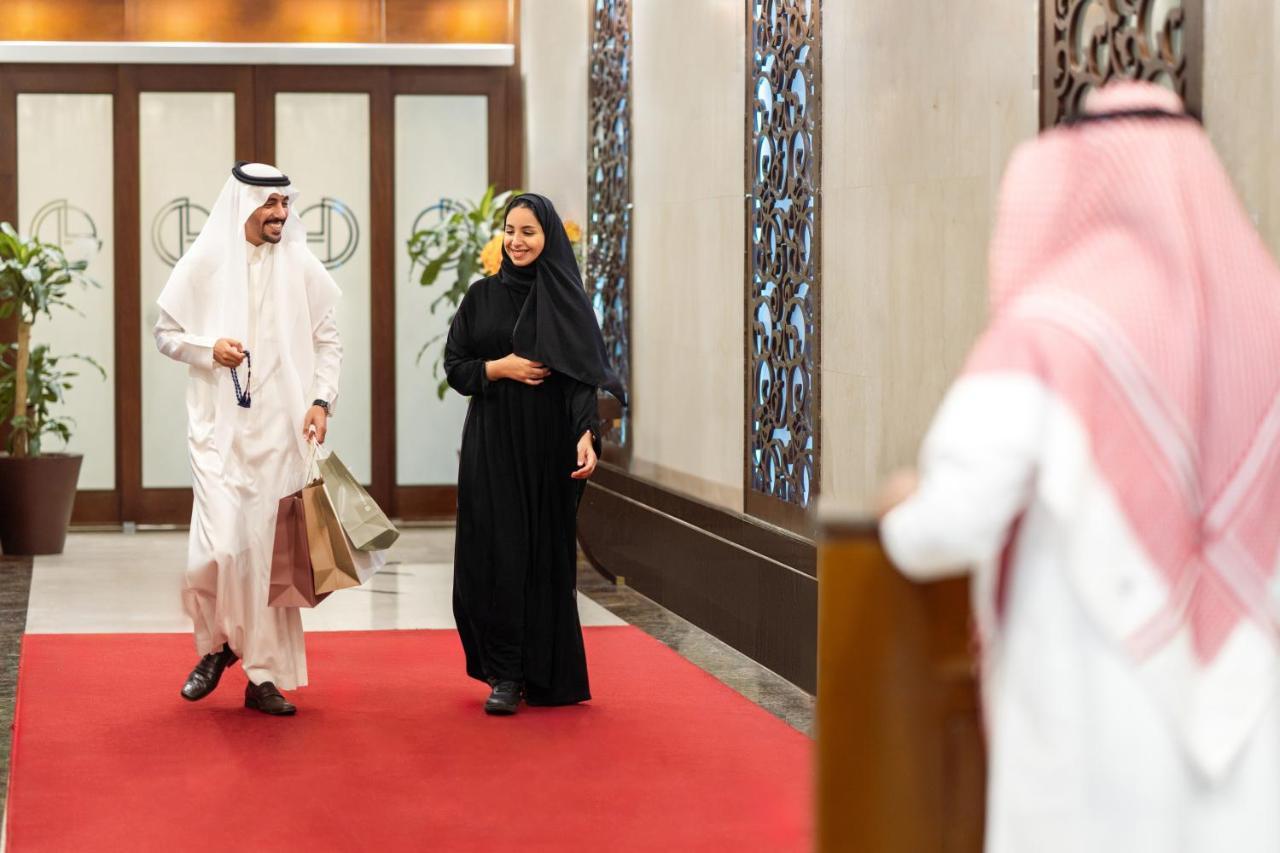 Makkah Clock Royal Tower, A Fairmont Hotel La La Mecca Esterno foto The photo depicts a scene inside a modern setting, possibly a hotel or a business environment. A man dressed in traditional attire, a white thobe and a headscarf, is walking beside a woman who is wearing a black abaya. They appear to be engaged in co