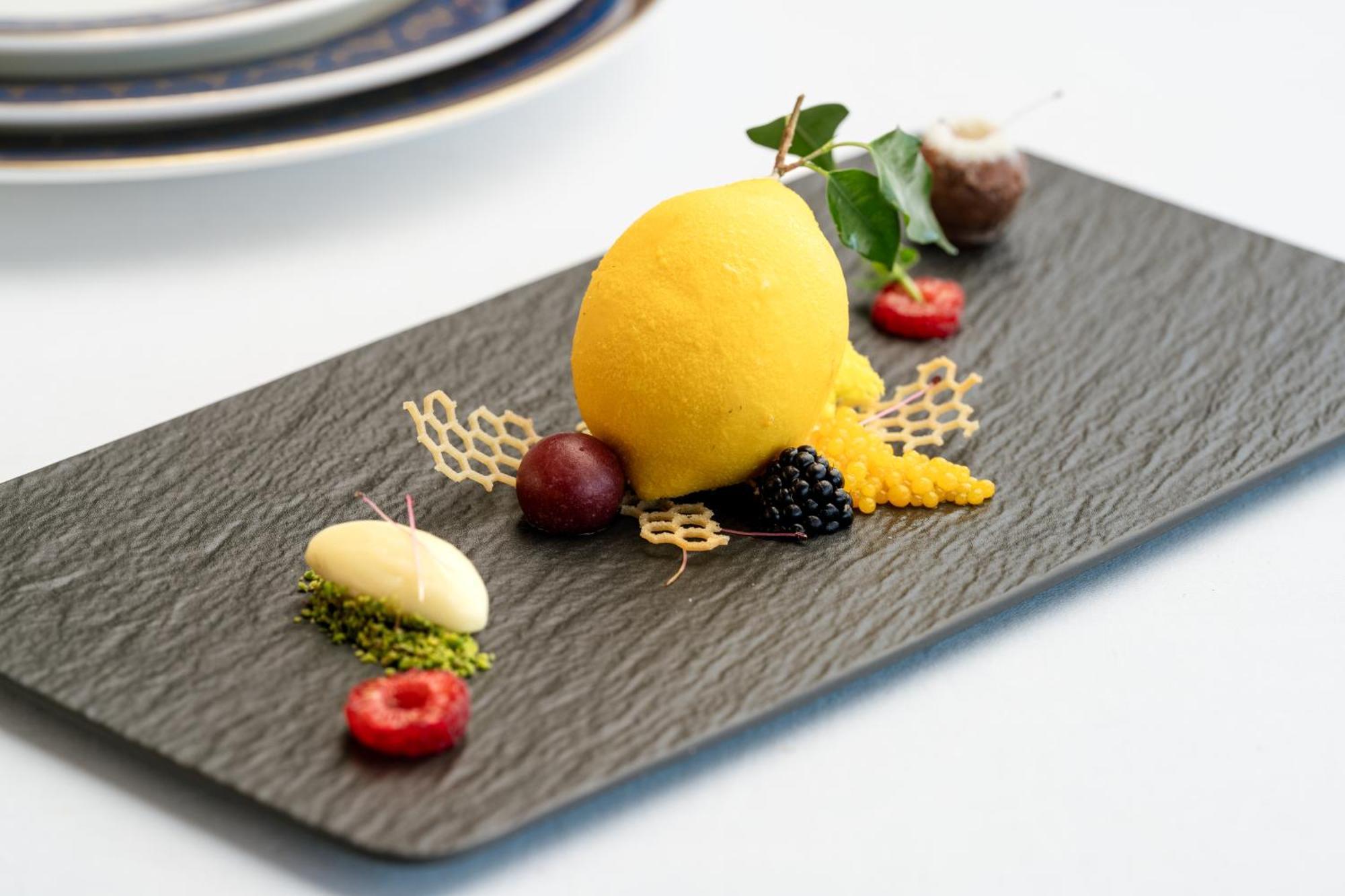 Makkah Clock Royal Tower, A Fairmont Hotel La La Mecca Esterno foto The photo displays an elegantly arranged dessert on a rectangular slate plate. The centerpiece is a vibrant yellow sorbet, shaped into a round scoop. Surrounding the sorbet are decorative elements, including:

- A lattice-like structure made of a cri