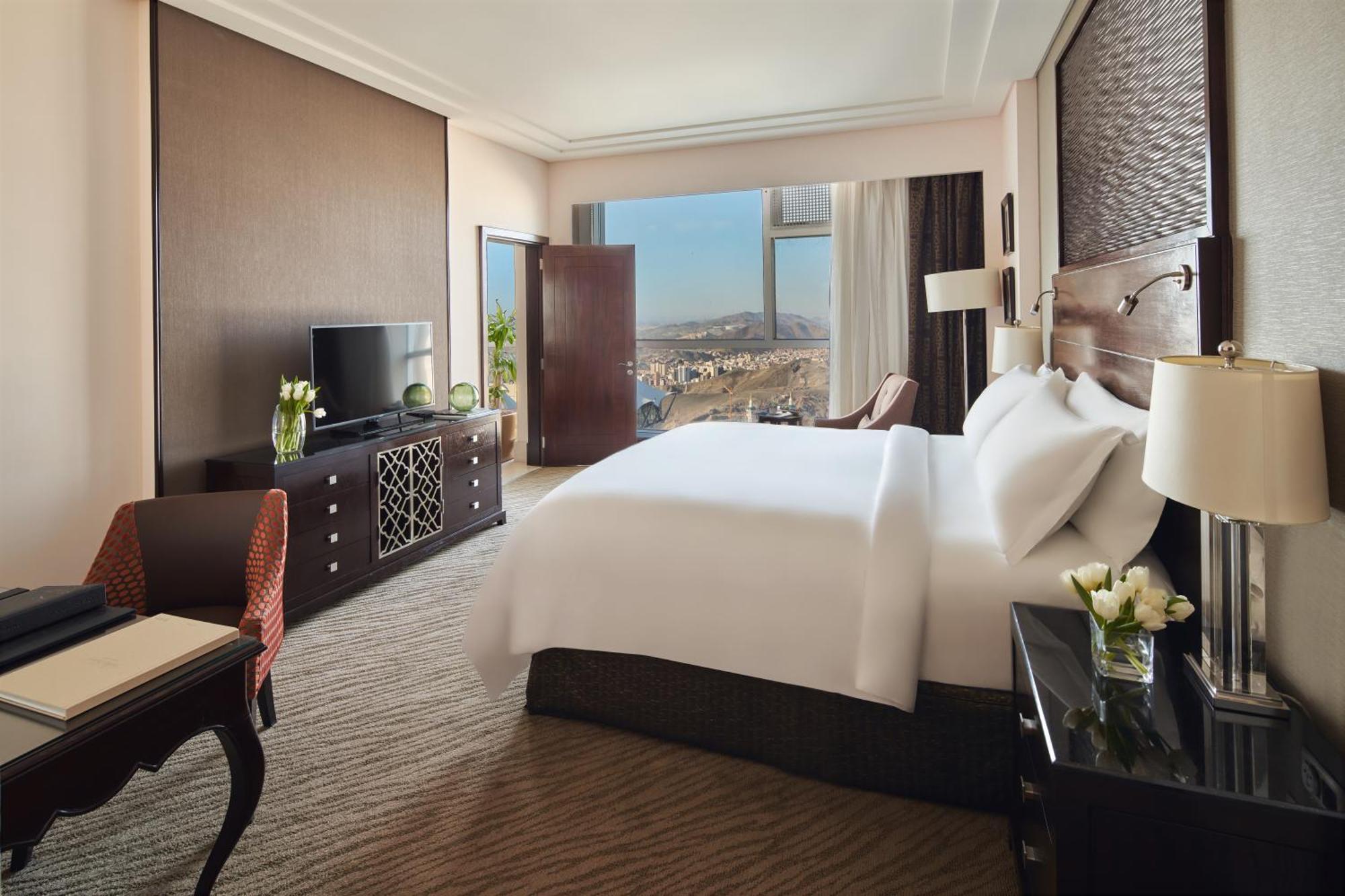 Makkah Clock Royal Tower, A Fairmont Hotel La La Mecca Esterno foto The photo shows a luxurious hotel room. It features a large bed with white linens, flanked by bedside tables with lamps. There is a stylish television unit opposite the bed, and large windows that provide a view of the outside landscape. The room has
