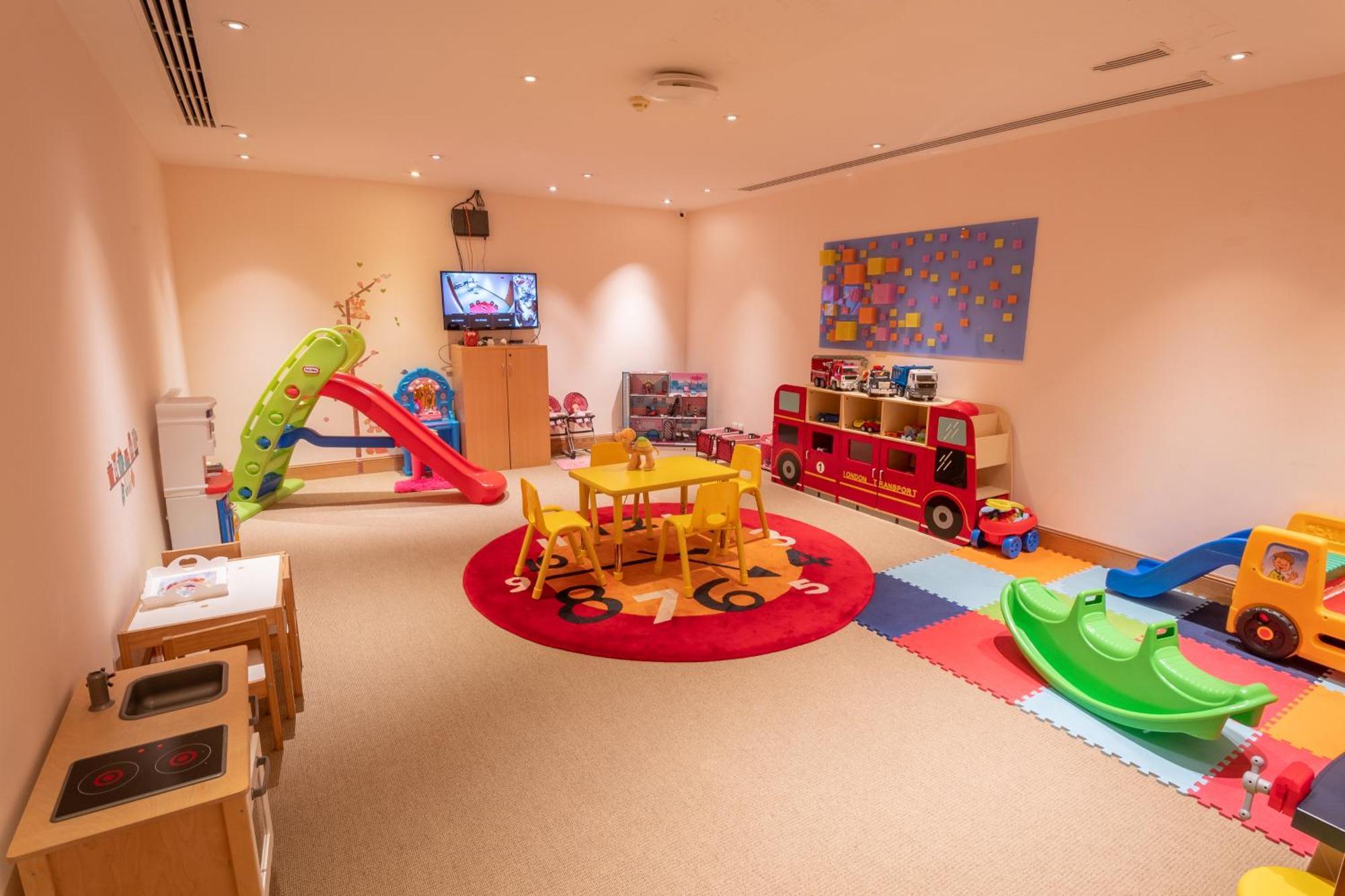 Makkah Clock Royal Tower, A Fairmont Hotel La La Mecca Esterno foto The photo shows a vibrant children's playroom. It features a colorful soft play area with a small slide and climbing structure. There's a bright red table surrounded by yellow chairs, suitable for activities or playtime. A large rug with a playful de