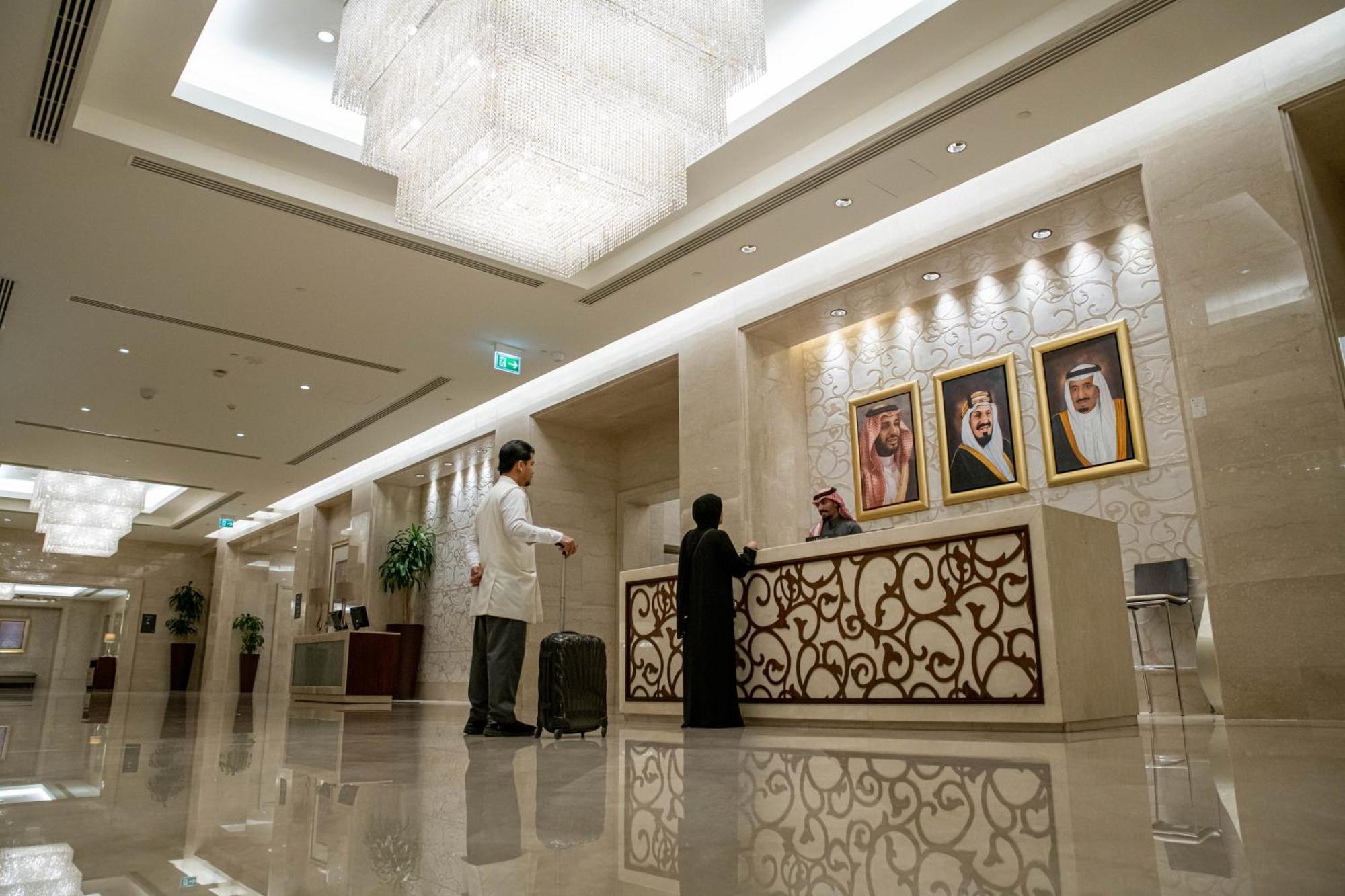 Makkah Clock Royal Tower, A Fairmont Hotel La La Mecca Esterno foto The photo shows the interior of a hotel lobby. There's a reception desk with an ornate design, and behind it, three framed portraits of individuals are displayed. A staff member, wearing a traditional outfit, is engaging with a guest who is standing 