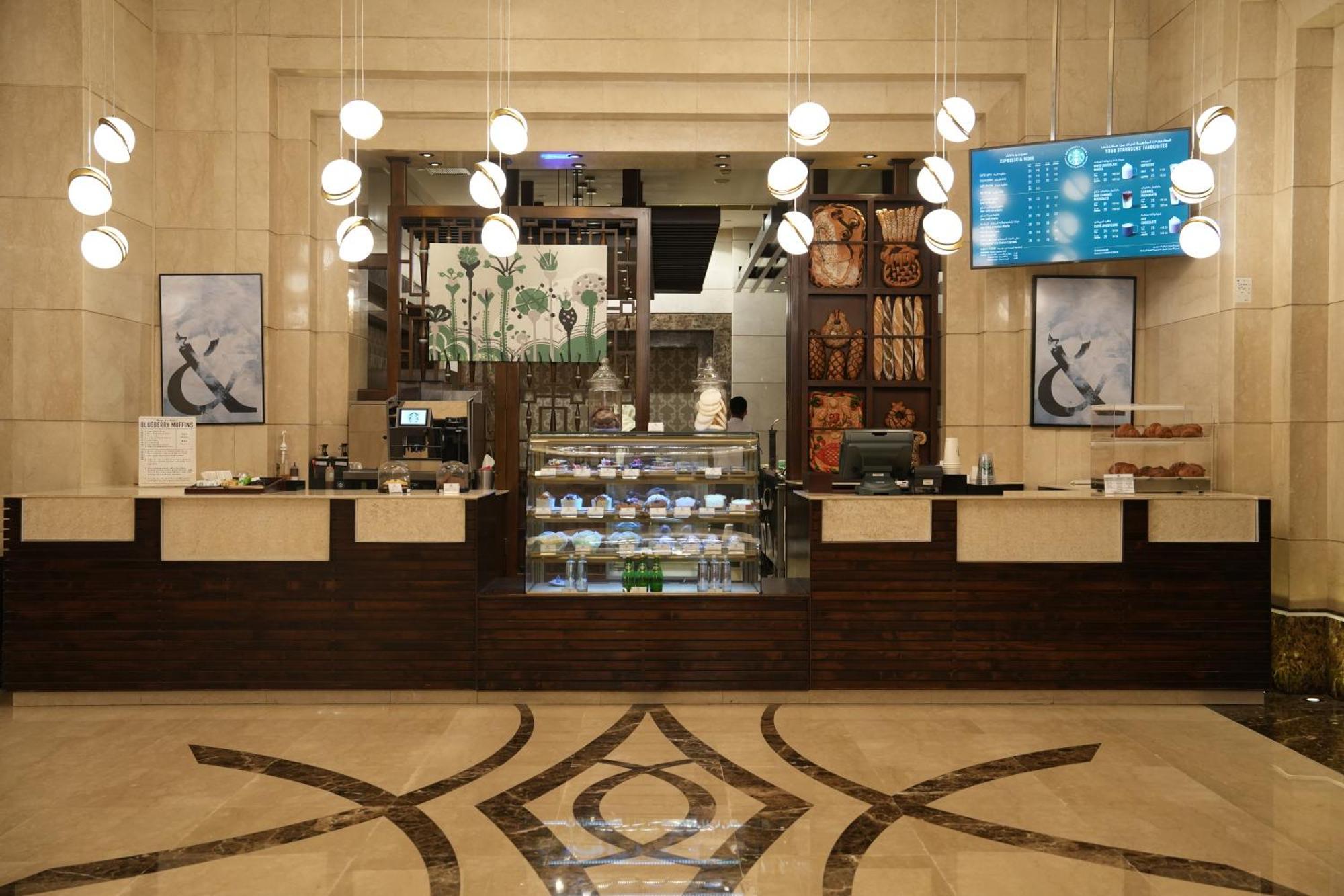 Makkah Clock Royal Tower, A Fairmont Hotel La La Mecca Esterno foto The photo shows an elegant café or reception area with a modern design. The front counter is sleek and made of light-colored materials, complemented by dark wooden accents. Behind the counter, there are shelves displaying various products, possibly b