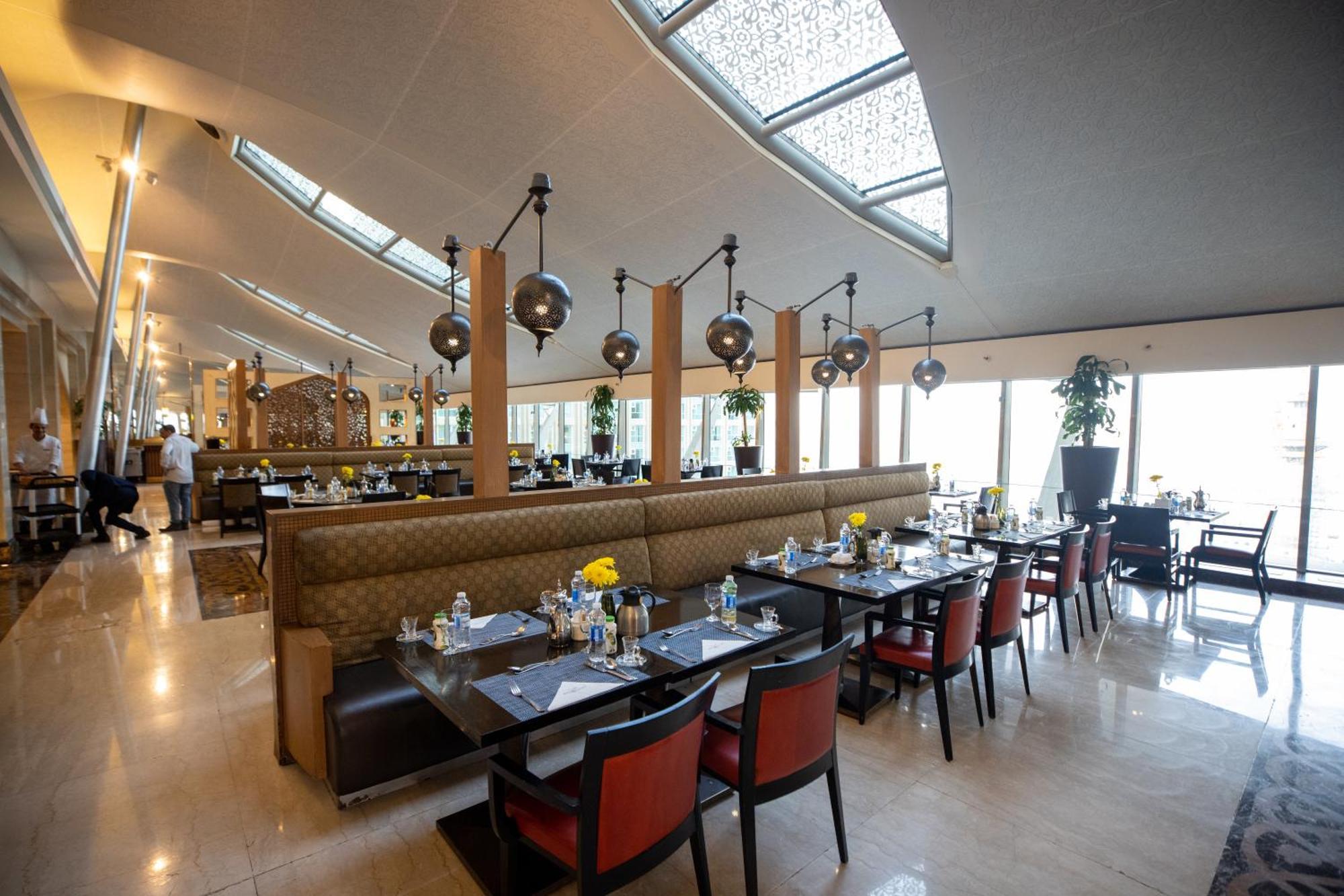 Makkah Clock Royal Tower, A Fairmont Hotel La La Mecca Esterno foto The photo shows a modern restaurant interior. There are several dining tables set with elegant tableware, including plates, glasses, and water bottles. The seating is a mix of black and red chairs, and some booths provide a more intimate dining exper