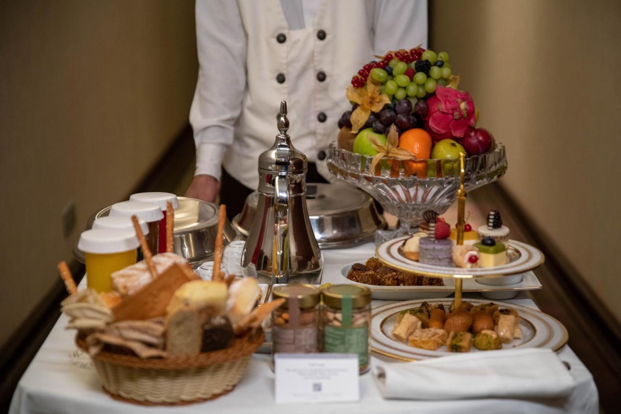 Makkah Clock Royal Tower, A Fairmont Hotel La La Mecca Esterno foto The photo shows a beautifully arranged display of food items on a table. There is a variety of fruit including grapes, oranges, and apples in an elegant bowl. In addition to the fruit, there are several trays and dishes featuring desserts and pastrie