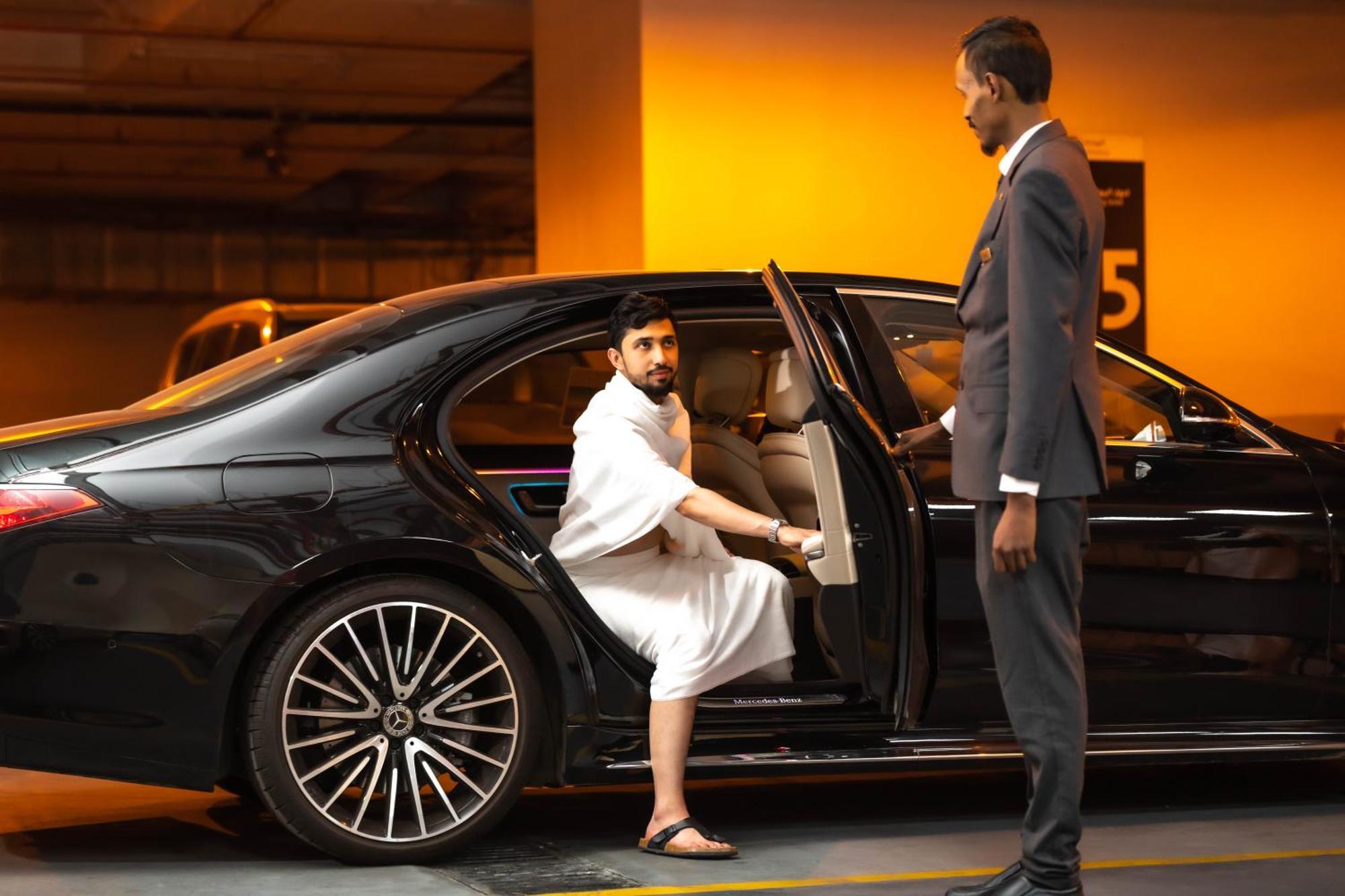 Makkah Clock Royal Tower, A Fairmont Hotel La La Mecca Esterno foto The photo shows a scene where a man, dressed in traditional attire, is seated in a luxury car. He appears to be getting out of the vehicle, with one leg already outside. A chauffeur or attendant in formal attire is standing beside the car, holding th