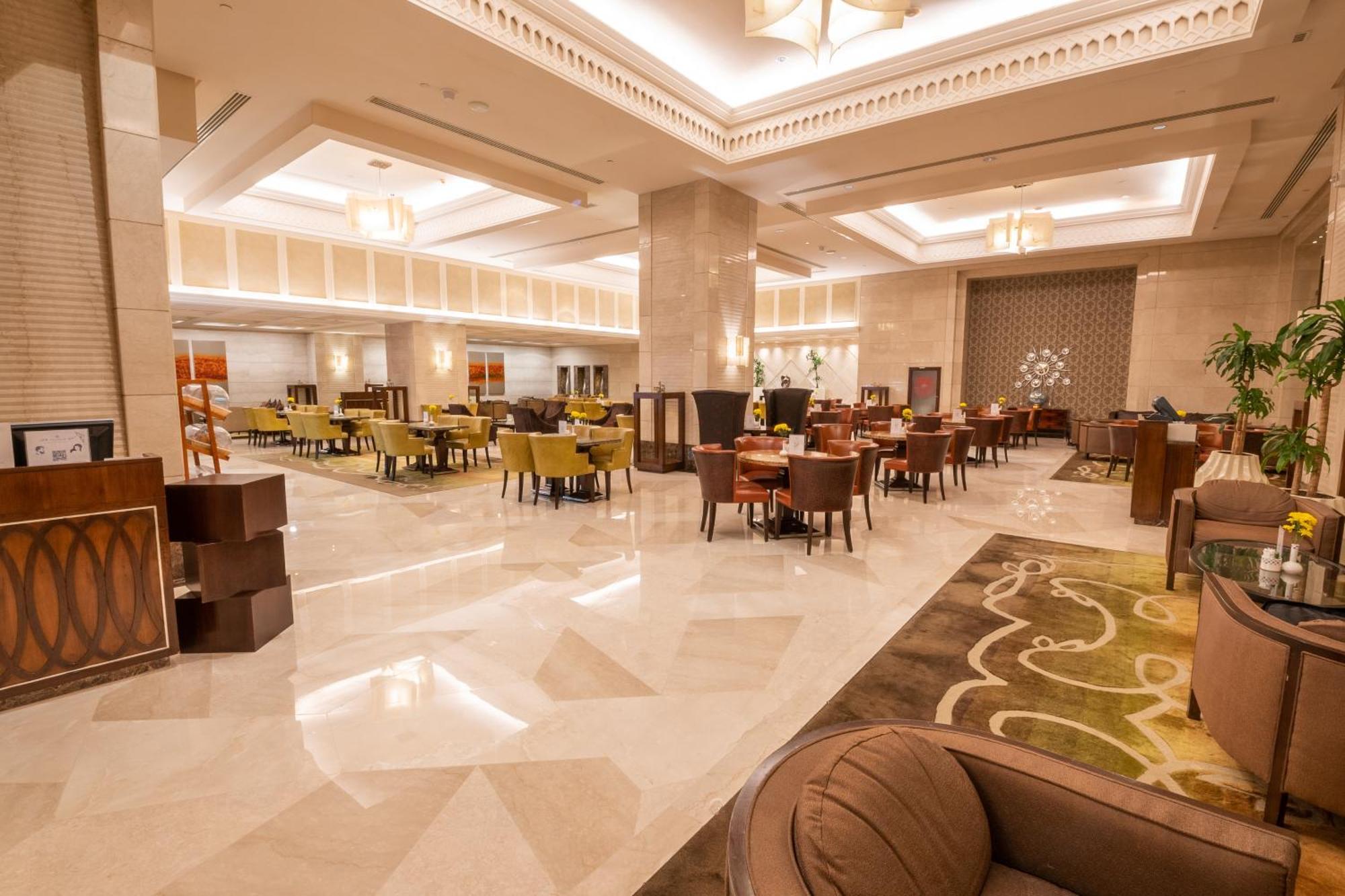 Makkah Clock Royal Tower, A Fairmont Hotel La La Mecca Esterno foto The photo shows the interior of a spacious dining area or lobby, featuring elegant design elements. The floor is made of polished marble, reflecting light from the overhead fixtures. There are numerous tables and chairs arranged throughout, with a mi