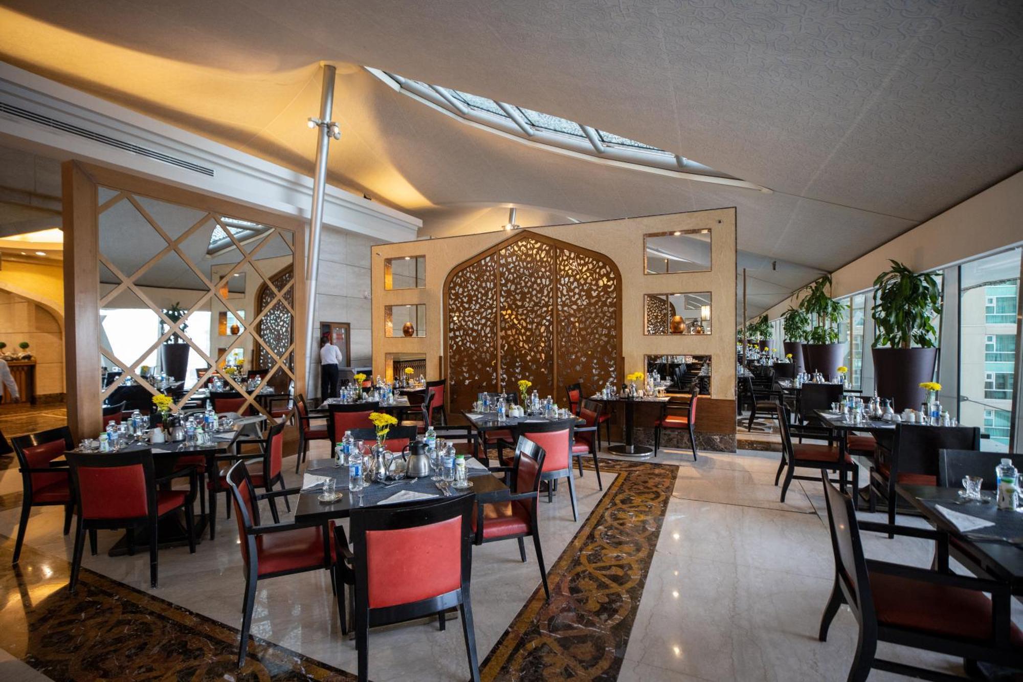 Makkah Clock Royal Tower, A Fairmont Hotel La La Mecca Esterno foto The photo depicts an elegant restaurant interior. It features tables set for dining with black tables and red chairs. The lighting is warm and inviting, enhanced by large windows that let in natural light from above. There are decorative elements lik