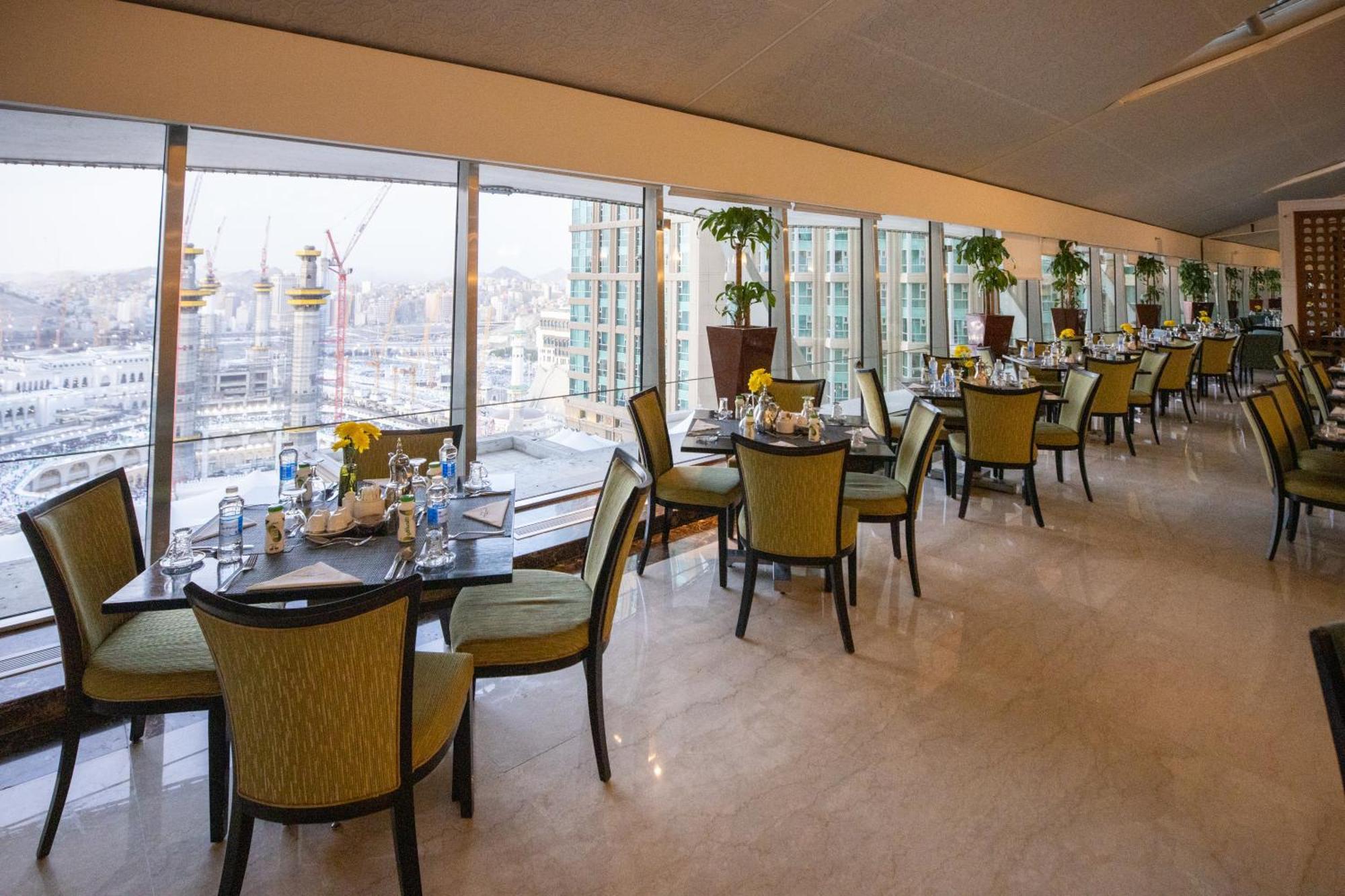 Makkah Clock Royal Tower, A Fairmont Hotel La La Mecca Esterno foto The photo features an elegant restaurant interior with a modern design. It showcases several dining tables, each set with tableware and a small flower arrangement. The chairs are green and have a stylish design. Large windows provide a panoramic view