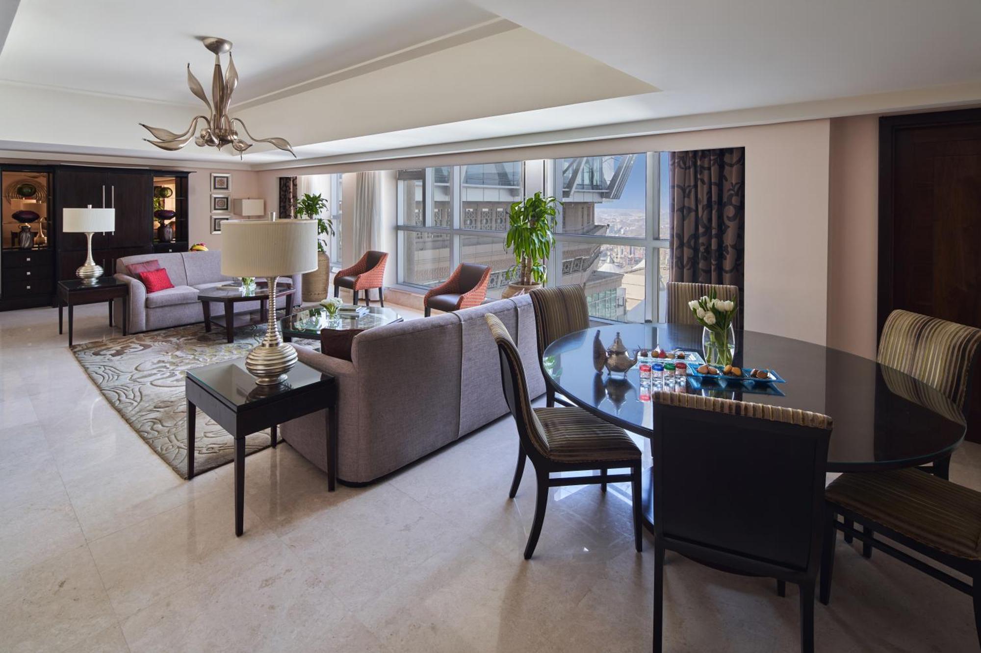 Makkah Clock Royal Tower, A Fairmont Hotel La La Mecca Esterno foto The photo shows a modern and elegantly designed living room and dining area. The space features large windows that let in natural light, with a view of the outside. There are two comfortable chairs and a sofa arranged around a coffee table, creating 
