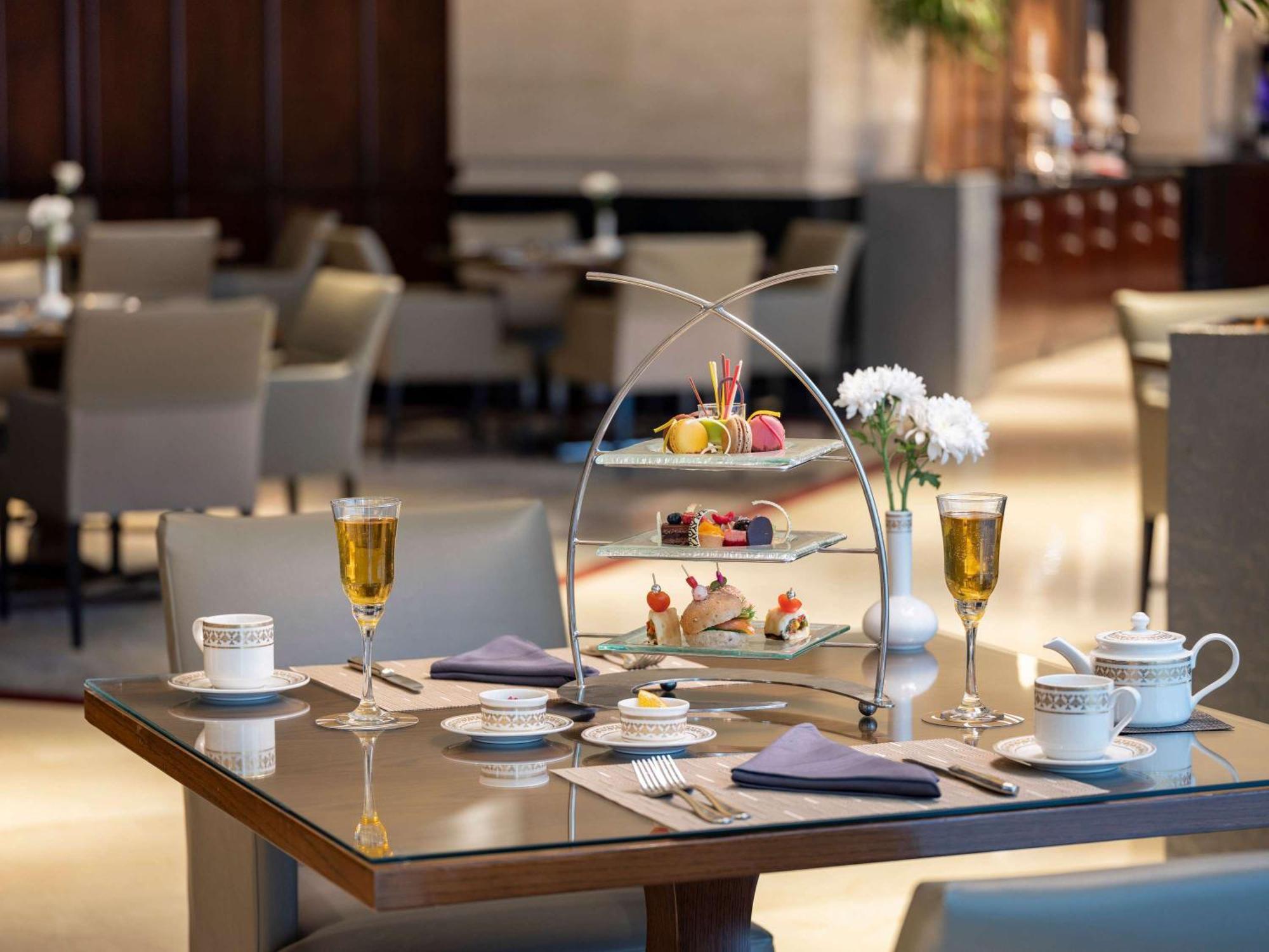 Makkah Clock Royal Tower, A Fairmont Hotel La La Mecca Esterno foto The photo depicts an elegantly arranged table setting in a restaurant. At the center, there is a multi-tiered stand filled with an assortment of colorful pastries and sweets, including macaroons and decorative cakes. Surrounding the stand, there are 