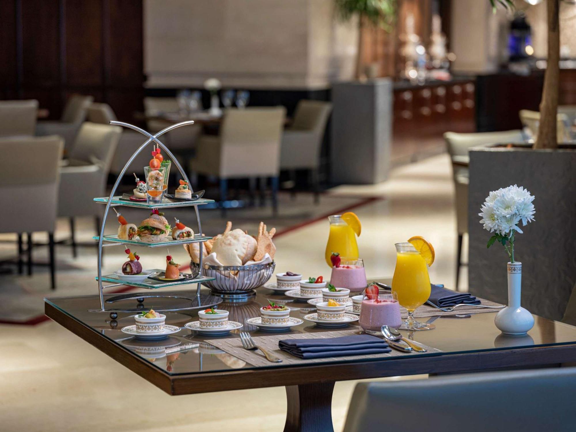 Makkah Clock Royal Tower, A Fairmont Hotel La La Mecca Esterno foto The photo shows a beautifully arranged table set for a lavish afternoon tea. There's a three-tiered stand featuring an assortment of pastries, sandwiches, and decorative treats, showcasing an elegant display of food. Additionally, there are small pla