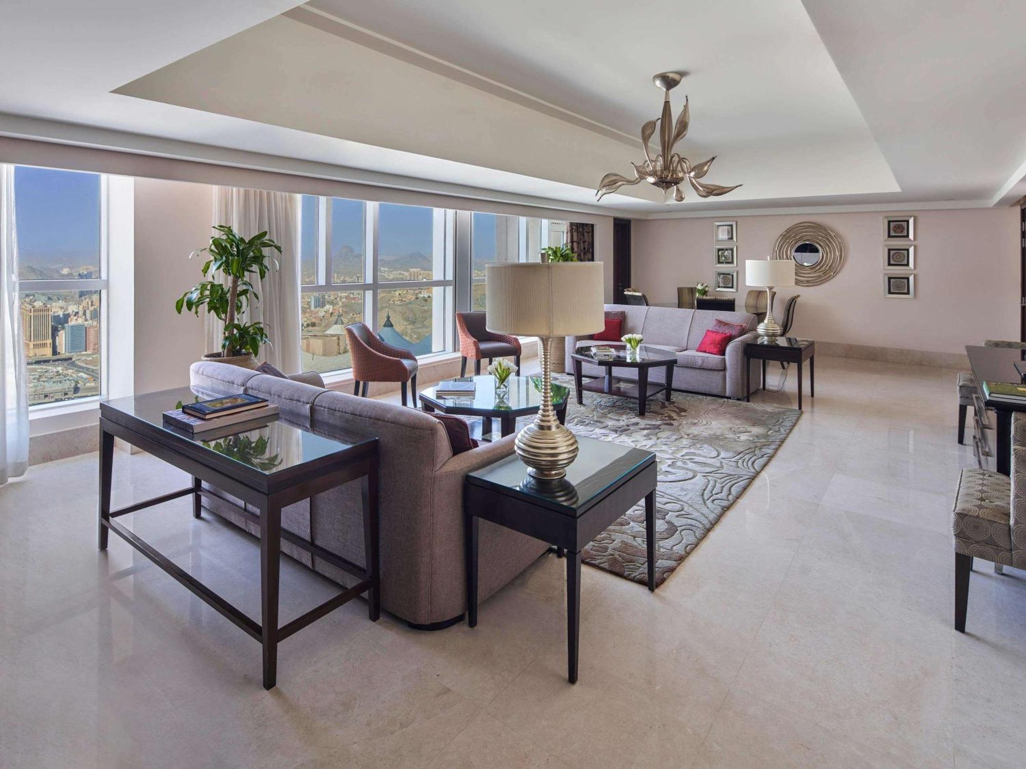 Makkah Clock Royal Tower, A Fairmont Hotel La La Mecca Esterno foto The photo shows a spacious, elegantly designed living room. It features large windows that allow natural light to flood the space and provide a view of the city. The room has a mix of comfortable seating arrangements, including a light-colored sofa s