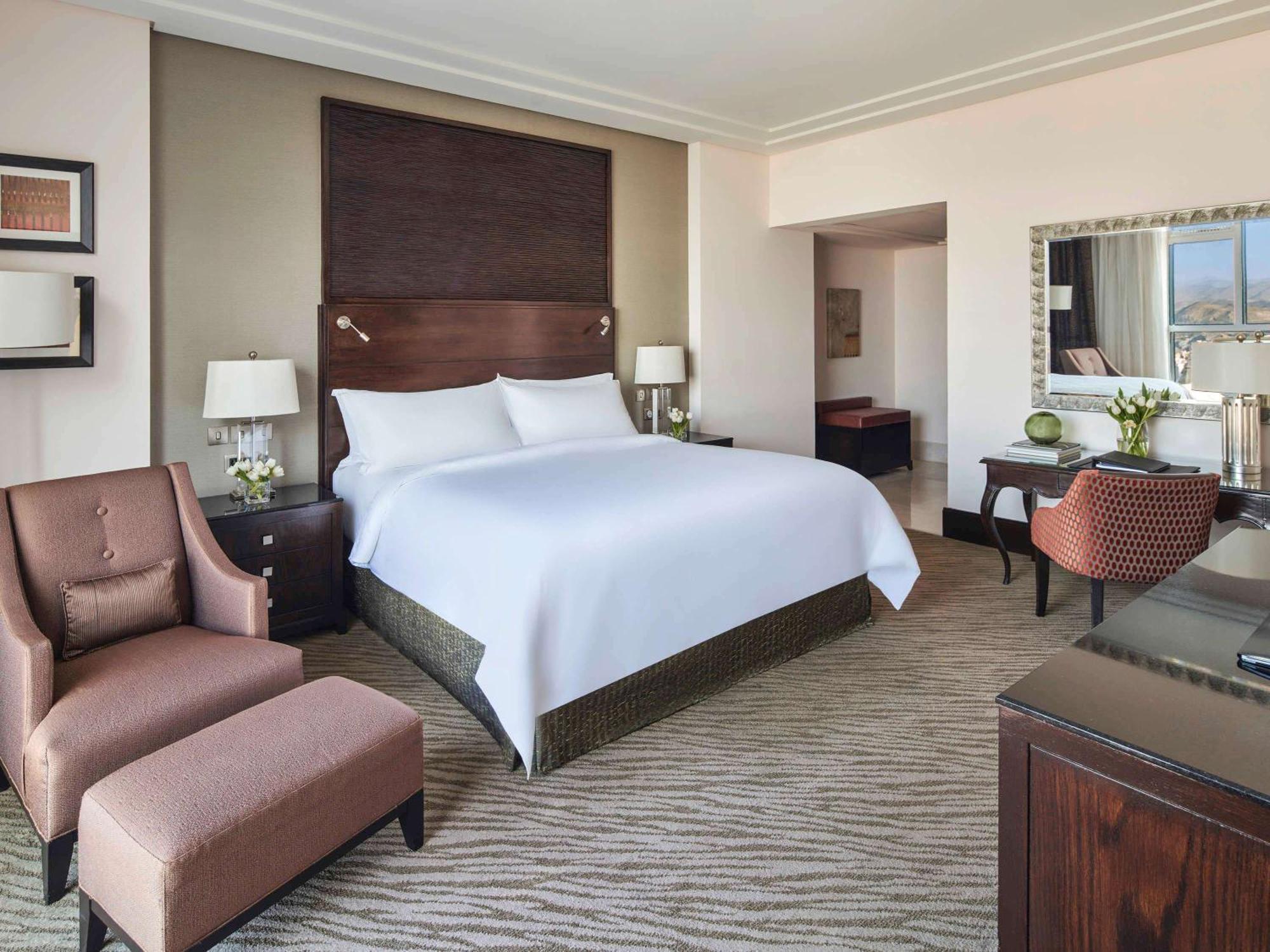 Makkah Clock Royal Tower, A Fairmont Hotel La La Mecca Esterno foto The photo shows a modern hotel room featuring a king-sized bed with a plush white duvet cover. On either side of the bed, there are stylish bedside tables with lamps. There are two comfortable armchairs—one is a single chair with an ottoman, and the 