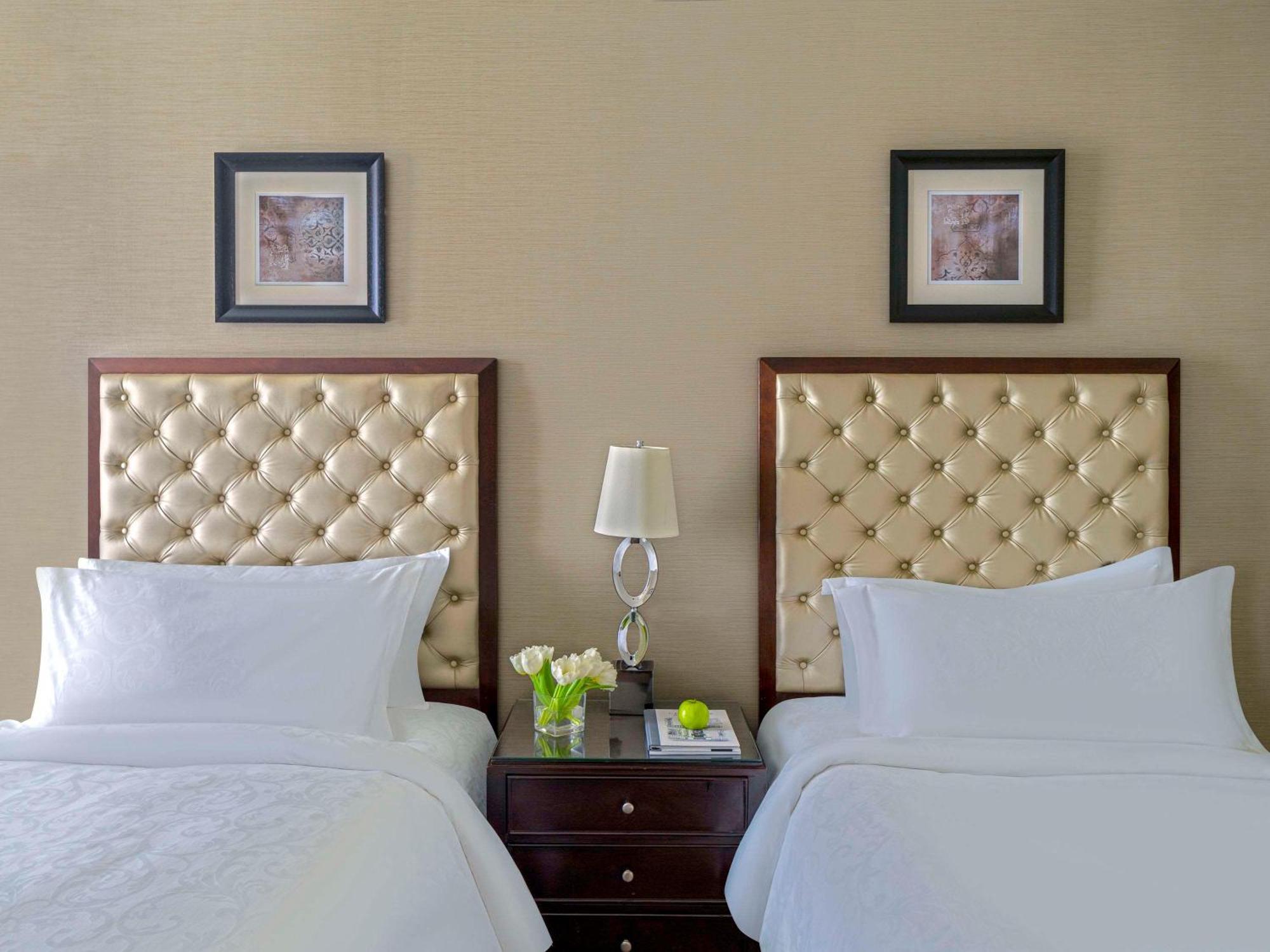 Makkah Clock Royal Tower, A Fairmont Hotel La La Mecca Esterno foto The photo shows a well-decorated room with two beds, each featuring a tufted headboard in a light fabric, and stylish bedding. A small nightstand is positioned between the beds, adorned with a decorative lamp and a couple of green flowers in a vase. 
