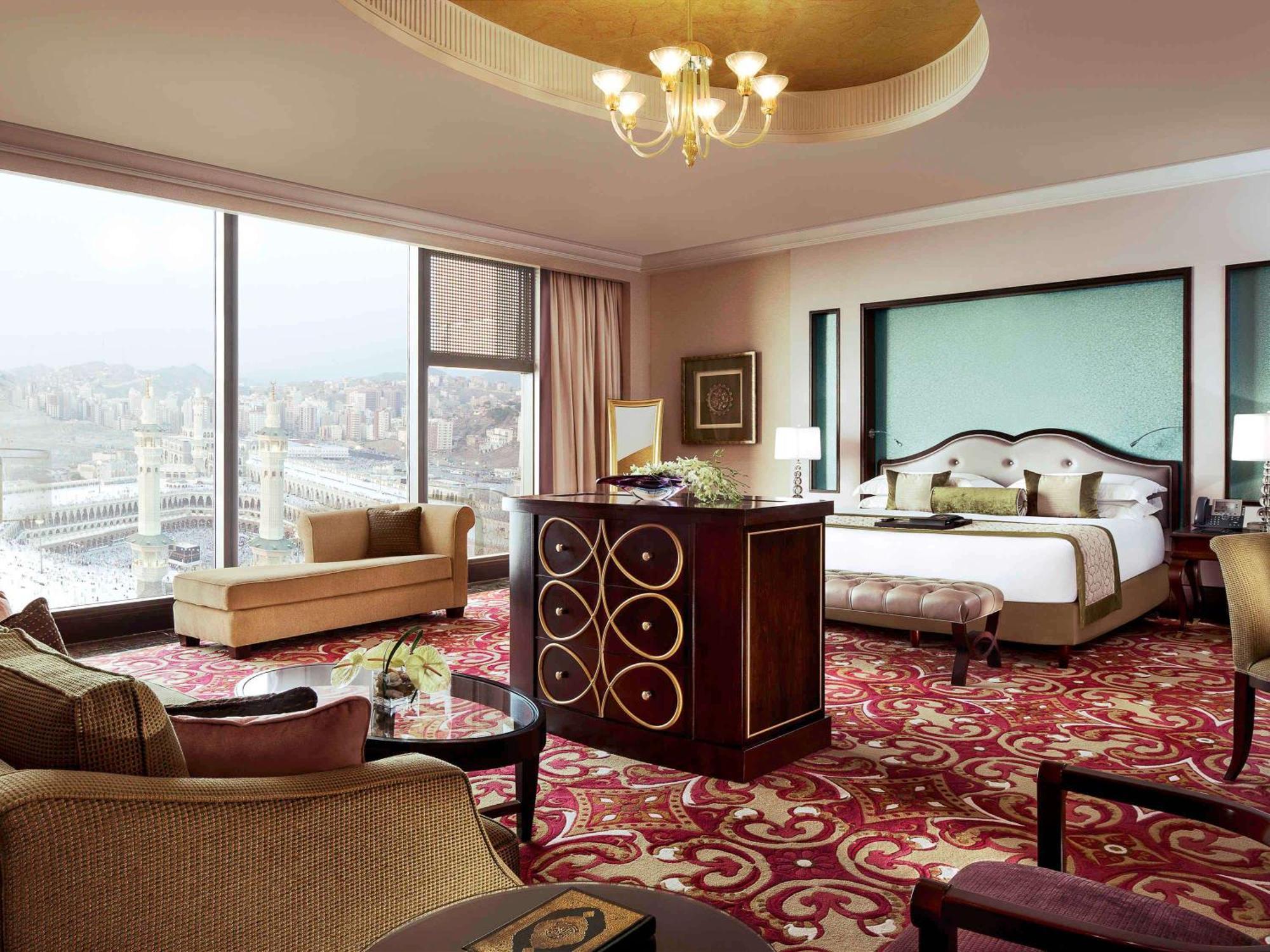 Makkah Clock Royal Tower, A Fairmont Hotel La La Mecca Esterno foto The photo shows a luxurious hotel room featuring elegant decor. The spacious room includes a large bed with plush bedding, a stylish seating area with a sofa, and a coffee table. There is a visually striking area rug on the floor, adding warmth and c